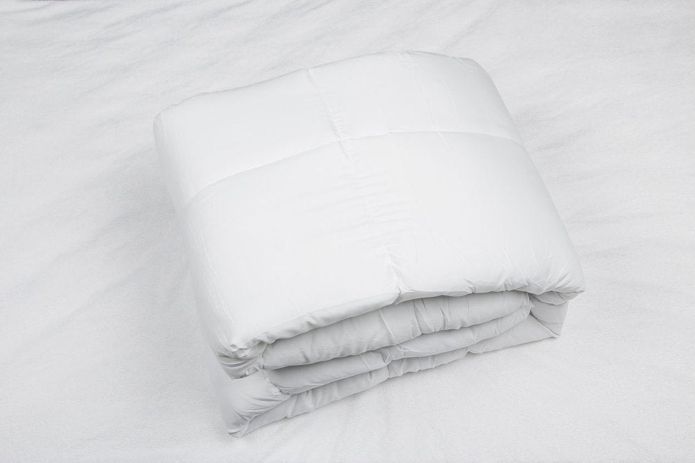A white microfiber duvet insert is folded on a white textured surface.