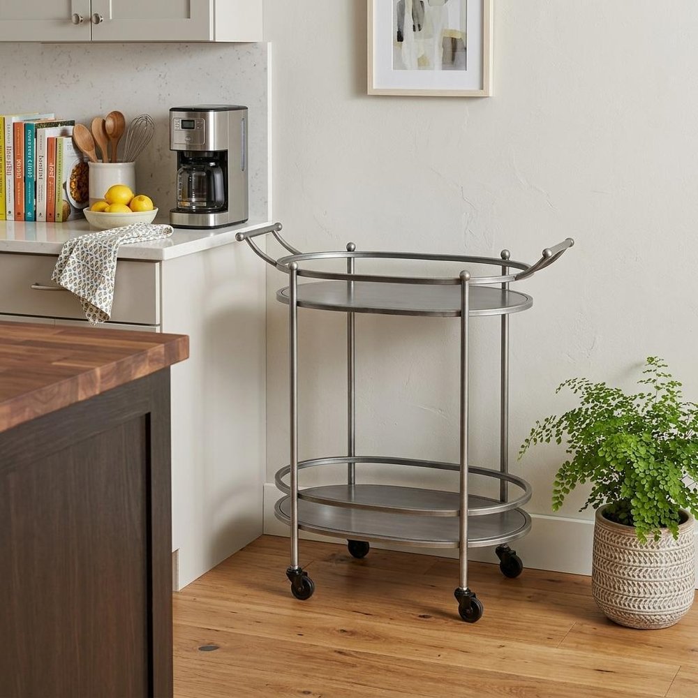 15 X 28 X 31 Bronze Antique Oval Service Cart styled in a furnished interior with a light gray wall on a wood floor in silver.