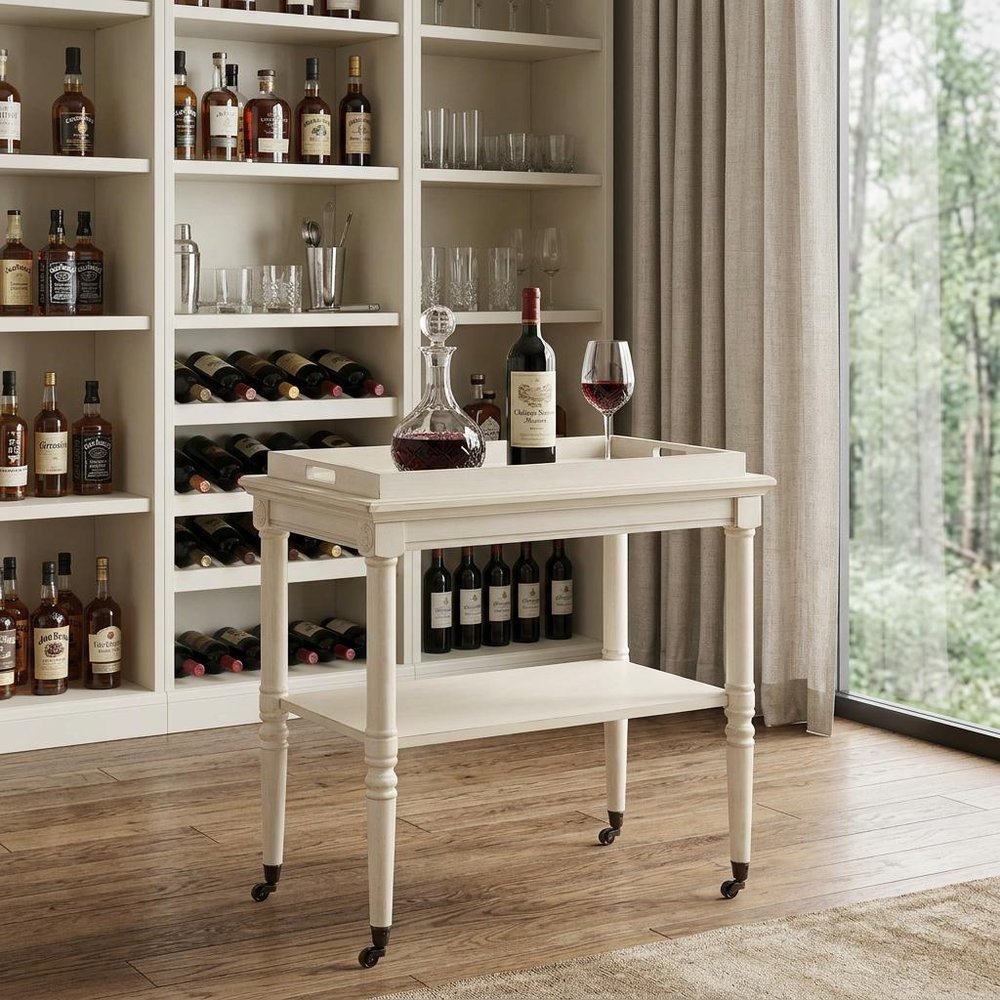 30" Antiqued White Wood Rolling Bar Cart styled in a furnished interior with a dark brown wall on a wood floor.
