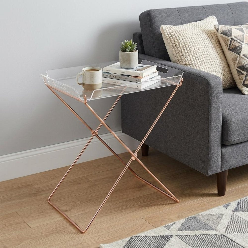 22" Clear and Copper Acrylic and Metal Tray Table styled in a furnished interior with an off-white wall on a wood floor.