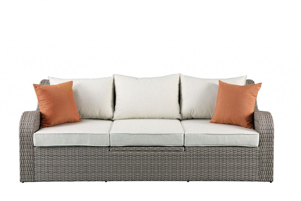 Gray wicker outdoor sectional sofa with beige seat cushions and three beige back cushions, two orange accent pillows on a white background.