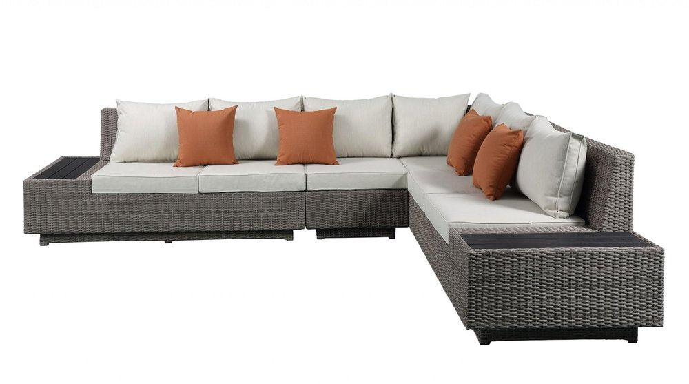 Gray wicker L-shaped sectional sofa with beige cushions and orange toss pillows on a white background.