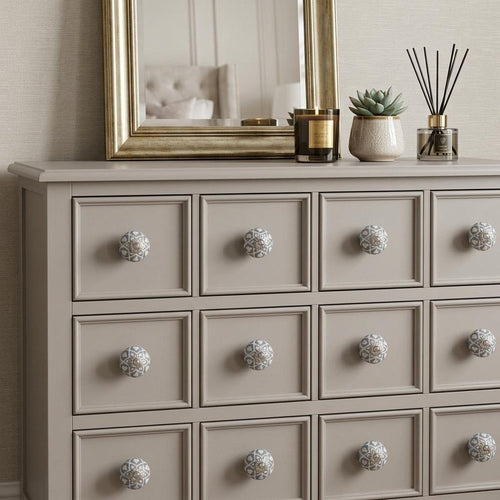 A beige dresser with twelve decorative blue and cream ceramic knobs, with a gold mirror and home decor items on top.