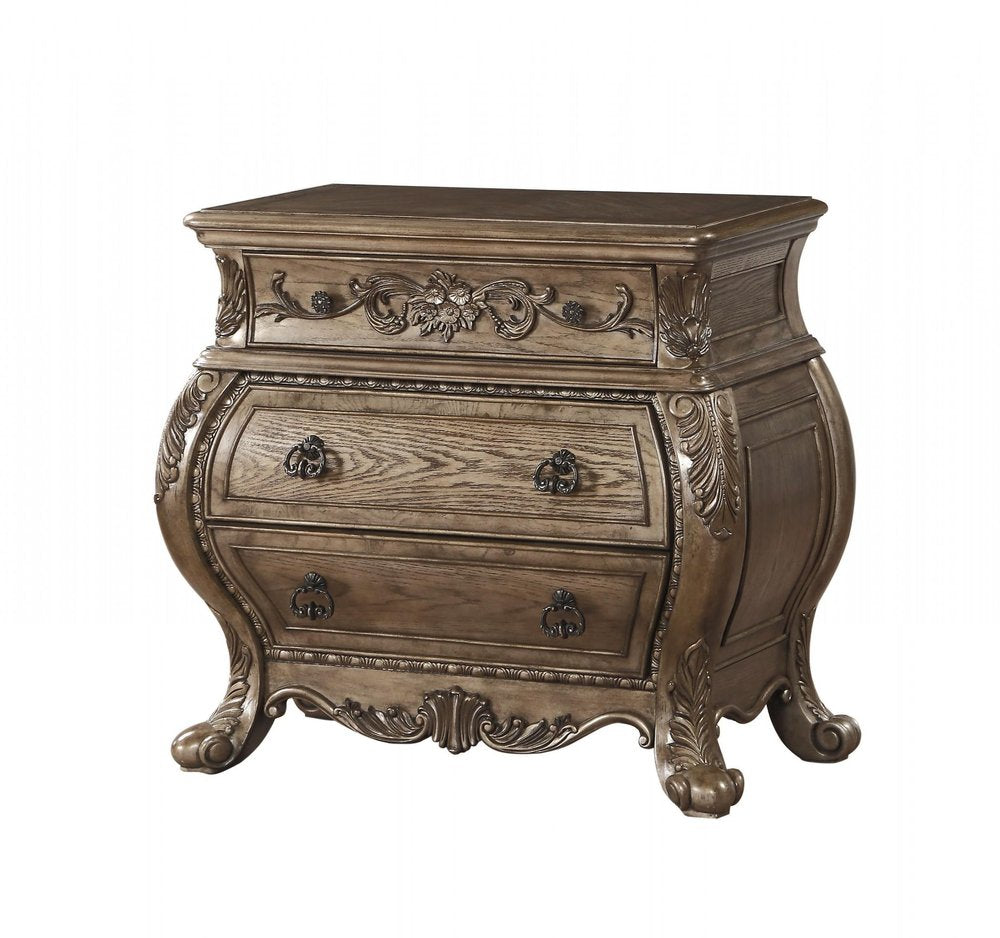 A brown solid wood nightstand with three drawers and ornate carvings sits on a white background.