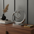 17" Silver Buffed Aluminum Modern Abstract Tabletop Sculpture styled in a furnished interior with a gray wall on a dark wood floor.