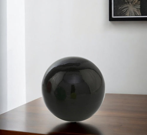 Black enameled aluminum decorative sphere on a wooden table with a white wall background.