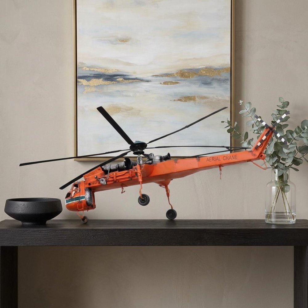 12" Orange Metal Hand Painted Model Airplane Tabletop Sculpture styled in a furnished interior with a tan wall on a dark wood floor.