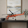 12" Orange Metal Hand Painted Model Airplane Tabletop Sculpture styled in a furnished interior with a tan wall on a dark wood floor.