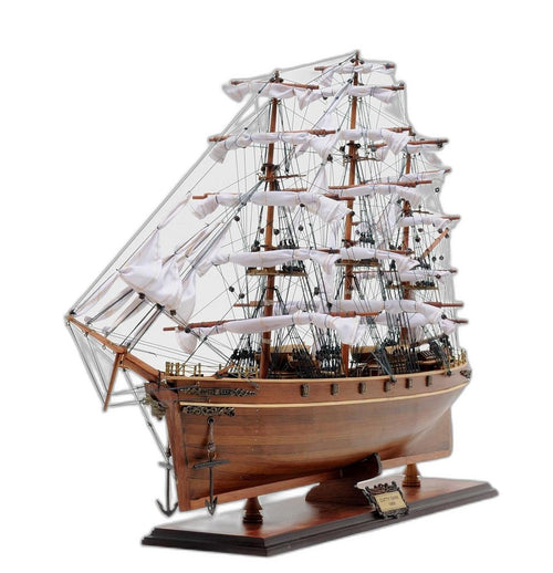 Wooden model of the Cutty Sark ship with white sails and brown hull on a wooden stand against a white background.