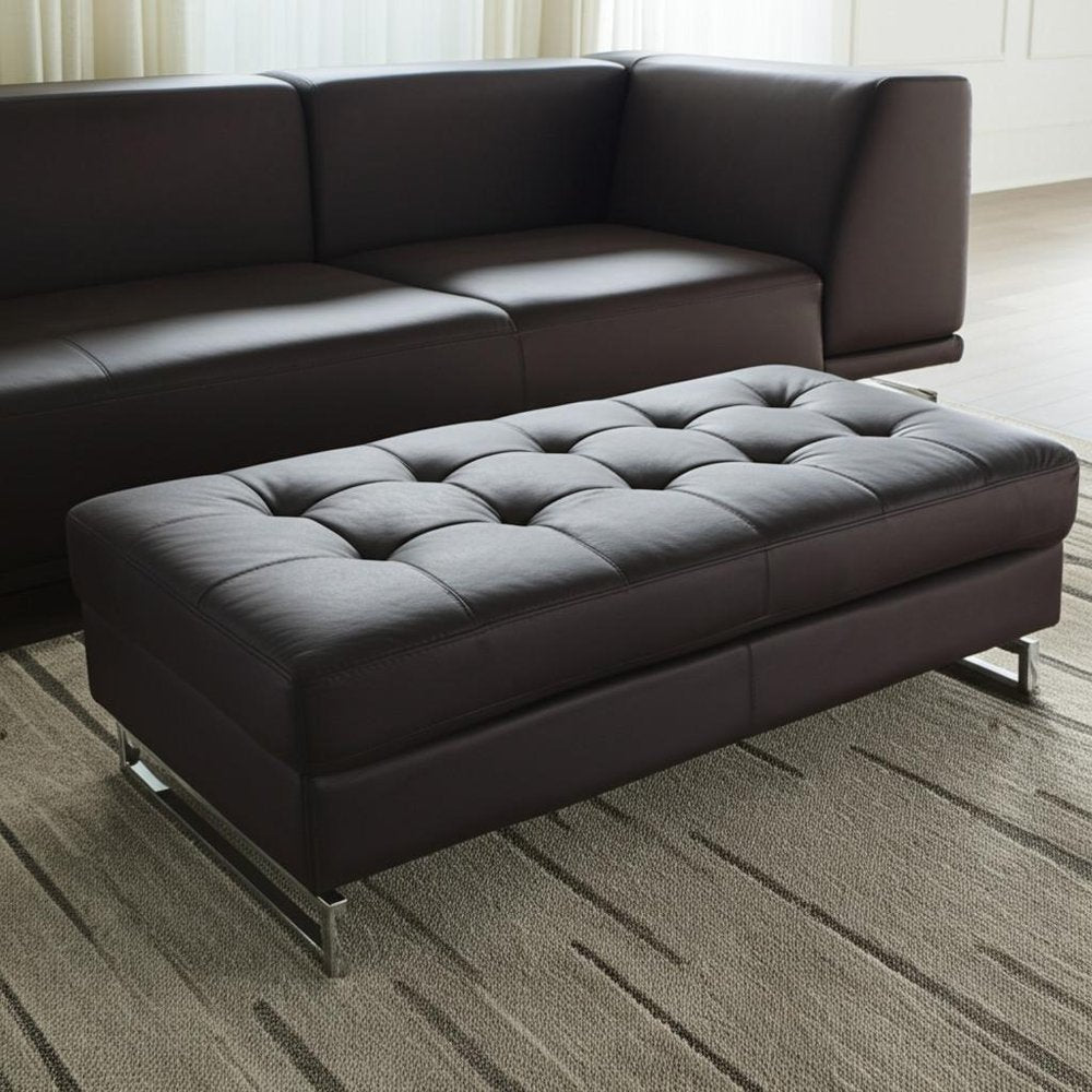 63" Brown and Silver Faux Leather Tufted Ottoman styled in a furnished interior with an off-white wall on a wood floor.
