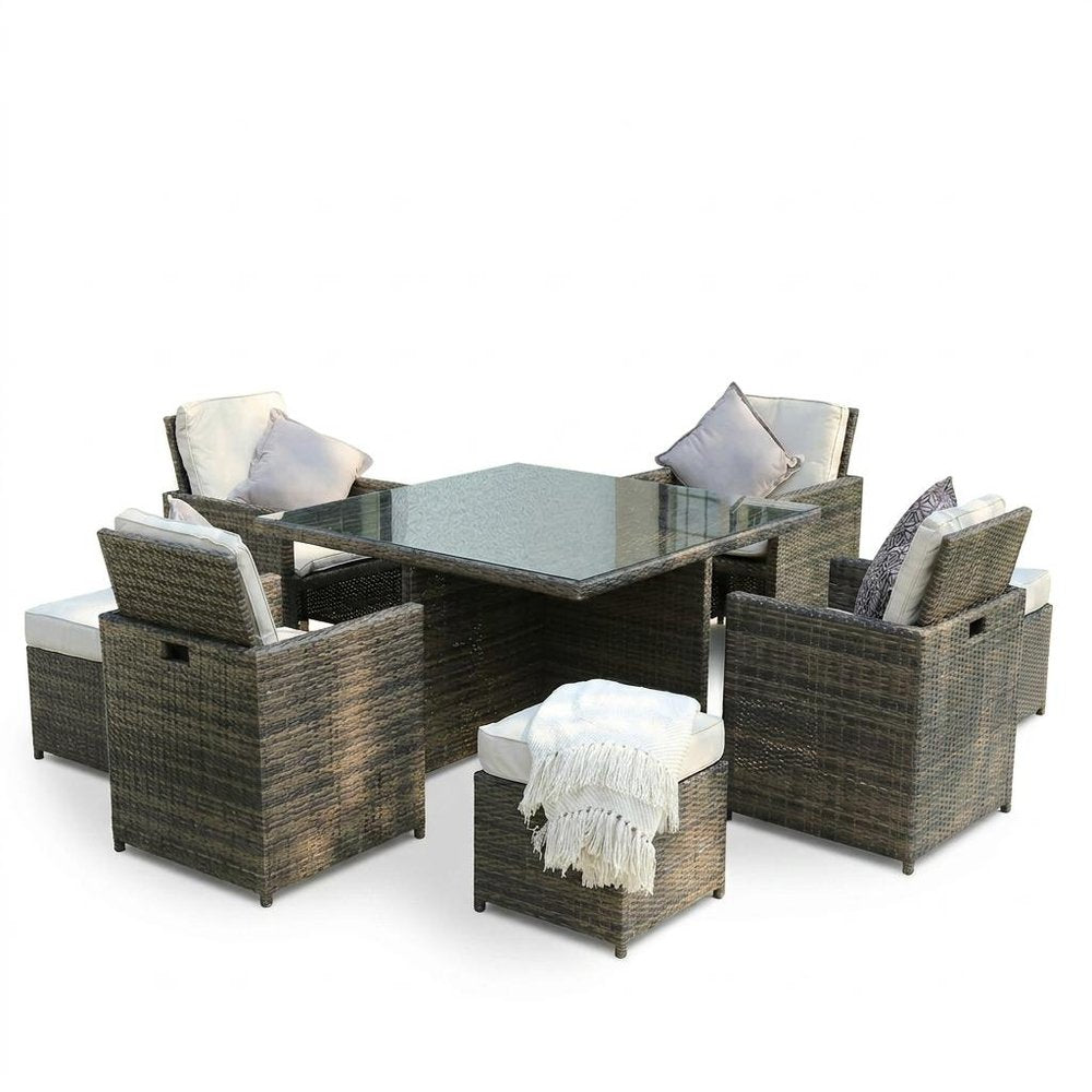 Wicker dining set with glass table, gray and white cushions, and white throw blanket on white background.