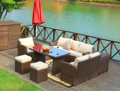 Brown wicker 7-piece outdoor sectional sofa with ottomans and storage box on a wooden deck overlooking a body of water.