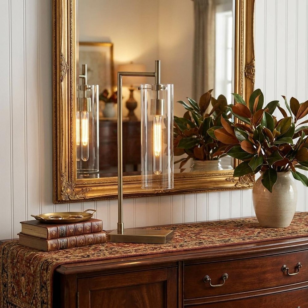 24" Brass Novelty With Clear Cylinder Shade styled in a furnished interior with a tan wall on a dark wood floor.
