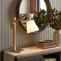 25" Natural Wood Adjustable Height Table Lamp With White Bell Shade displayed on a dark wood tabletop in a furnished interior against a dark brown wall in tan wood.
