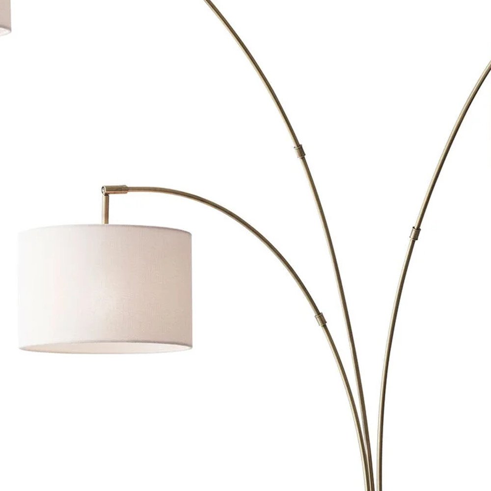 74" Brass Three Light Arc Floor Lamp With Off White Fabric Drum Shade on a white background