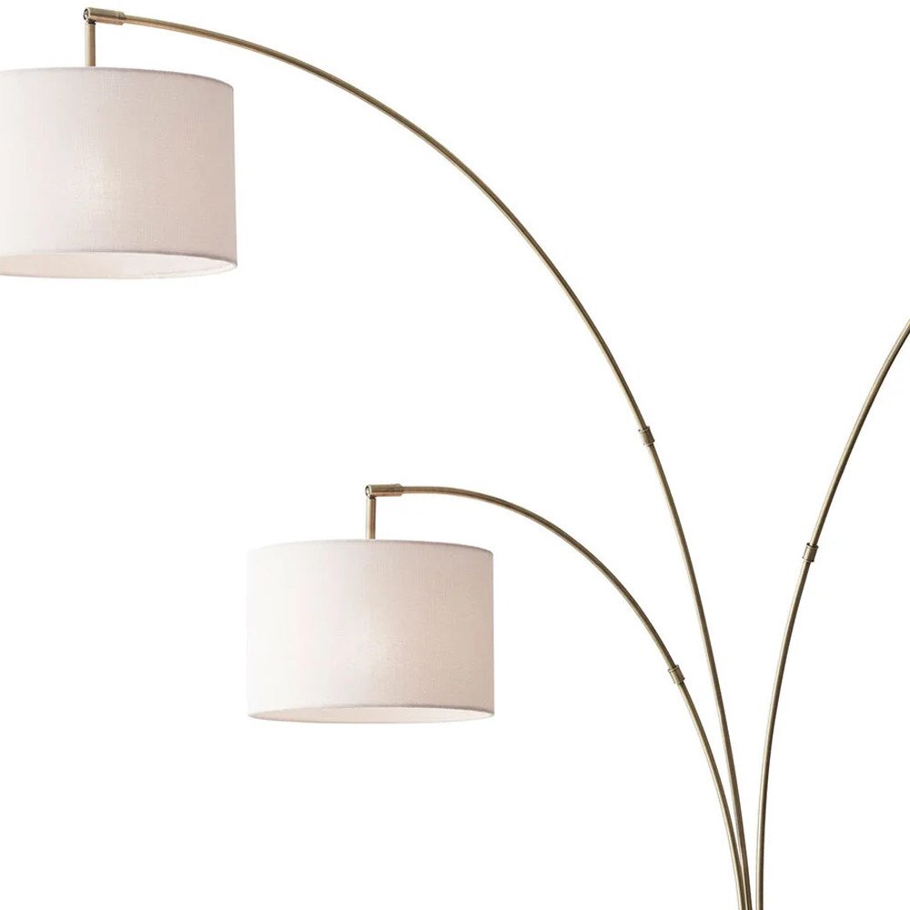 74" Brass Three Light Arc Floor Lamp With Off White Fabric Drum Shade on a white background