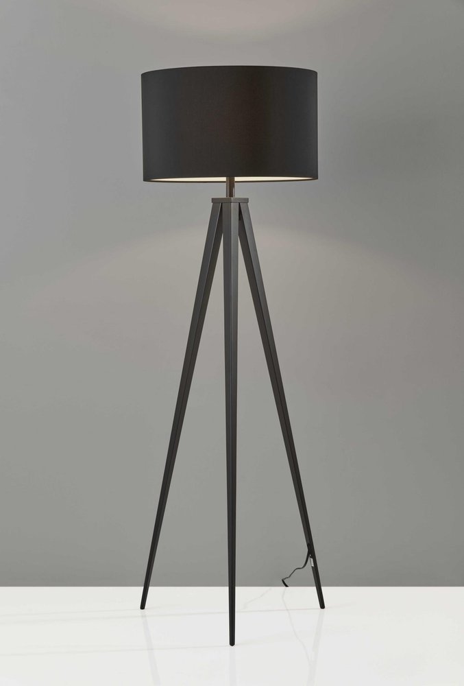 Black metal tripod floor lamp with a black fabric drum shade against a grey background.