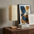 25" Natural Solid Wood And Silver Metal Table Lamp Beige Paper Shade displayed on a dark wood tabletop in a furnished interior against a tan wall.