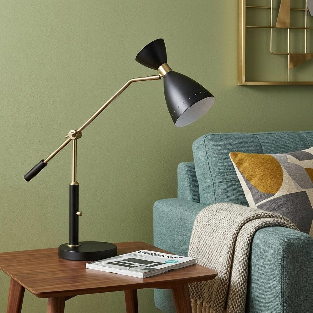 32" Black And Gold Metal Desk Lamp With Cinched Cone Shade styled in a furnished interior with a gold wall on a dark wood floor.