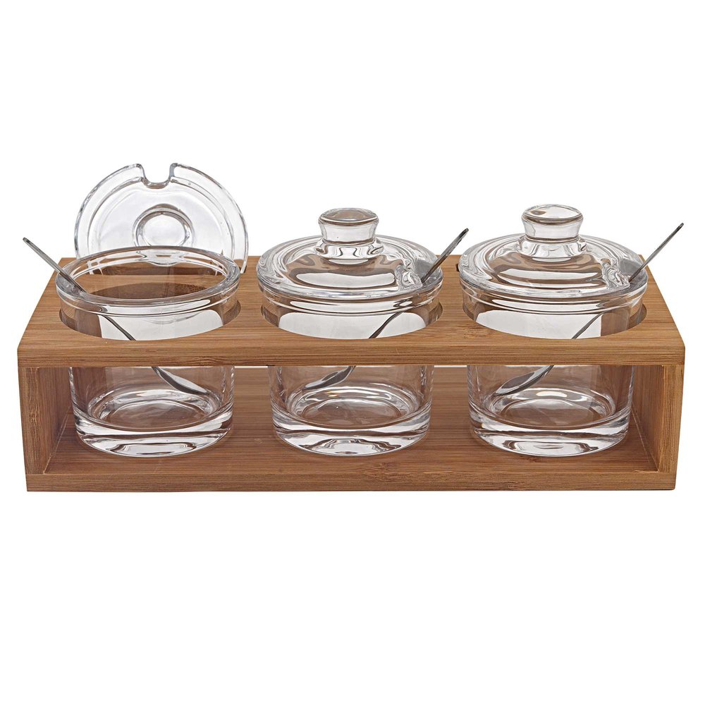 Three clear glass jam jars with lids and spoons sit in a wooden stand.