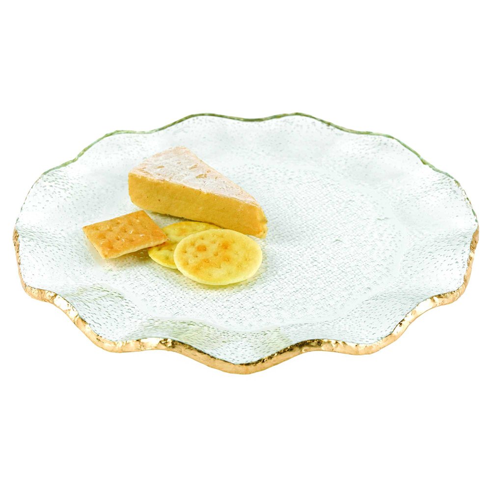 A clear glass platter with a wavy gold edge holds a slice of cheese and crackers on a white background.