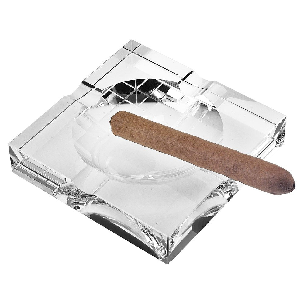 Clear crystal square cigar ashtray with a cigar resting on it, isolated on a white background.