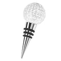 Clear crystal golf ball bottle stopper with silver metal base and black rubber rings on a white background.
