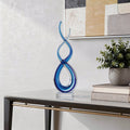 20" Clear and Blue Murano Glass Modern Abstract Tabletop Sculpture styled in a furnished interior with an off-white wall on a off-white floor.