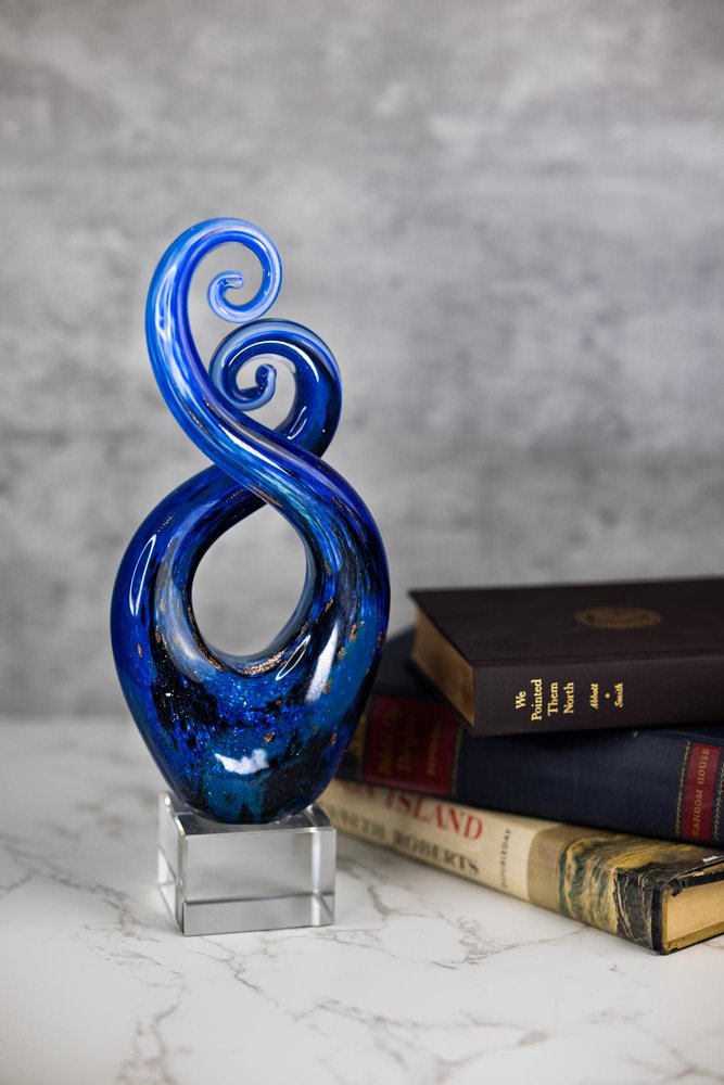 12" Blue and Green Murano Glass Modern Abstract Tabletop Sculpture styled in a furnished interior with a light gray wall on a off-white floor.
