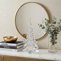 10" Mouth Blown Clear Glass Christmas Tree Sculpture styled in a furnished interior with an off-white wall on a off-white floor.