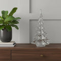 12" Mouth Blown Clear Glass Christmas Tree Sculpture styled in a furnished interior with a light gray wall on a dark wood floor.