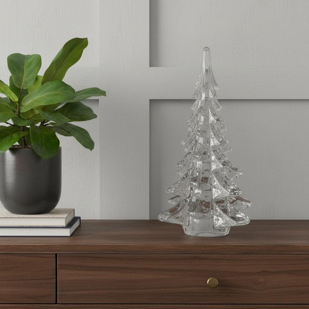 12" Mouth Blown Clear Glass Christmas Tree Sculpture styled in a furnished interior with a light gray wall on a dark wood floor.