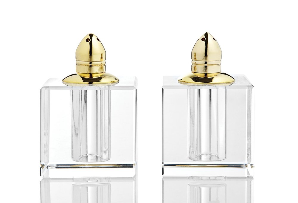 Two clear crystal pepper shakers with gold tops on a white background.