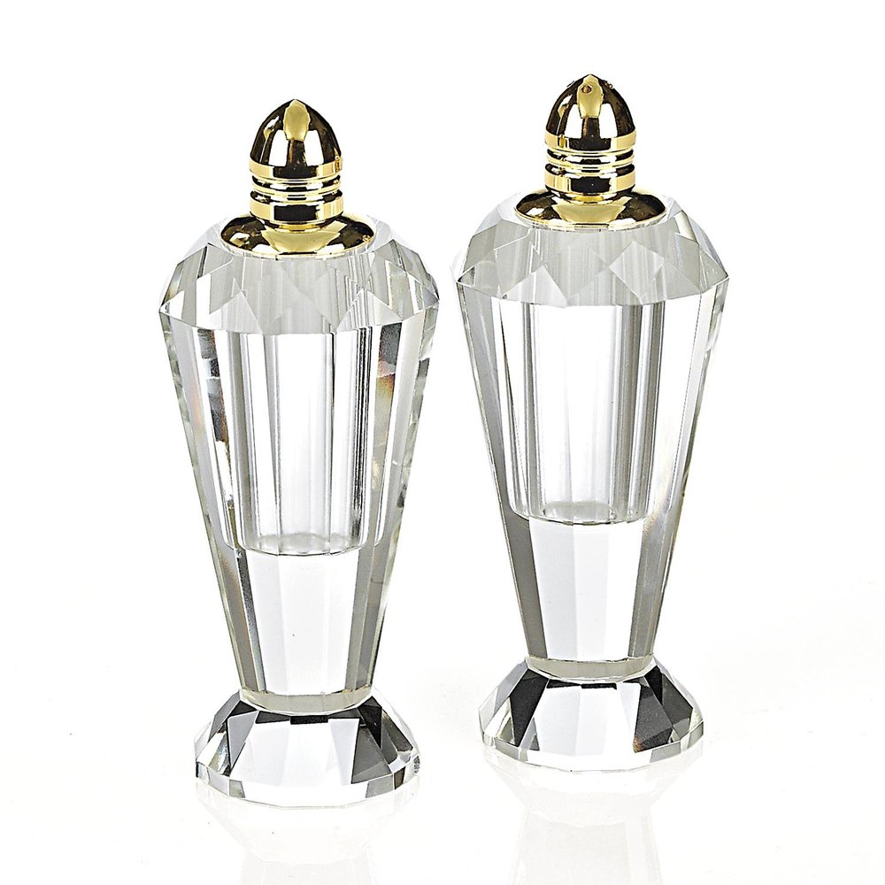 Two clear crystal geometric pepper shakers with gold caps on a white background.