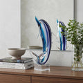 14" Blue Murano Glass Dolphin Figurine Tabletop Sculpture styled in a furnished interior with an off-white wall on a dark wood floor.