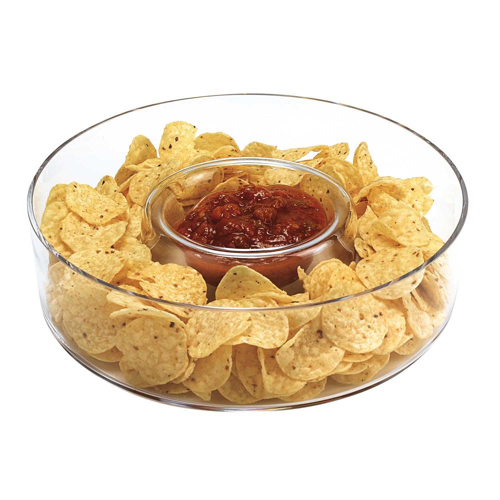 Clear glass chip and dip bowl filled with tortilla chips and salsa on a white background.