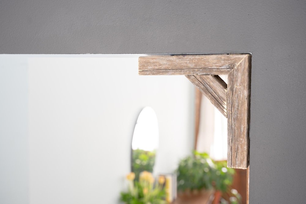 Close-up of a weathered gray wooden corbel attached to a mirror frame against a gray wall.
