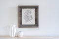Gray solid wood tabletop picture frame with a black line drawing of a fern leaf on a white background, displayed on a wooden surface.