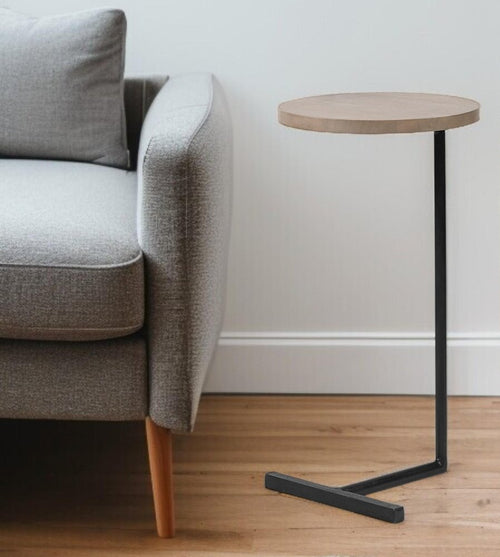 Round natural wood top C-table with black metal base next to a grey sofa on a wood floor.