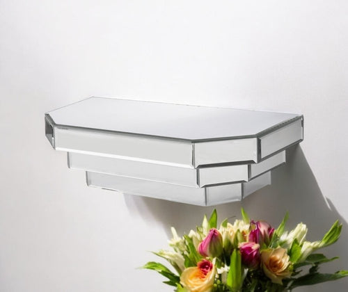 A silver mirrored glass dimensional floating shelf mounted on a white wall with a bouquet of flowers in the foreground.