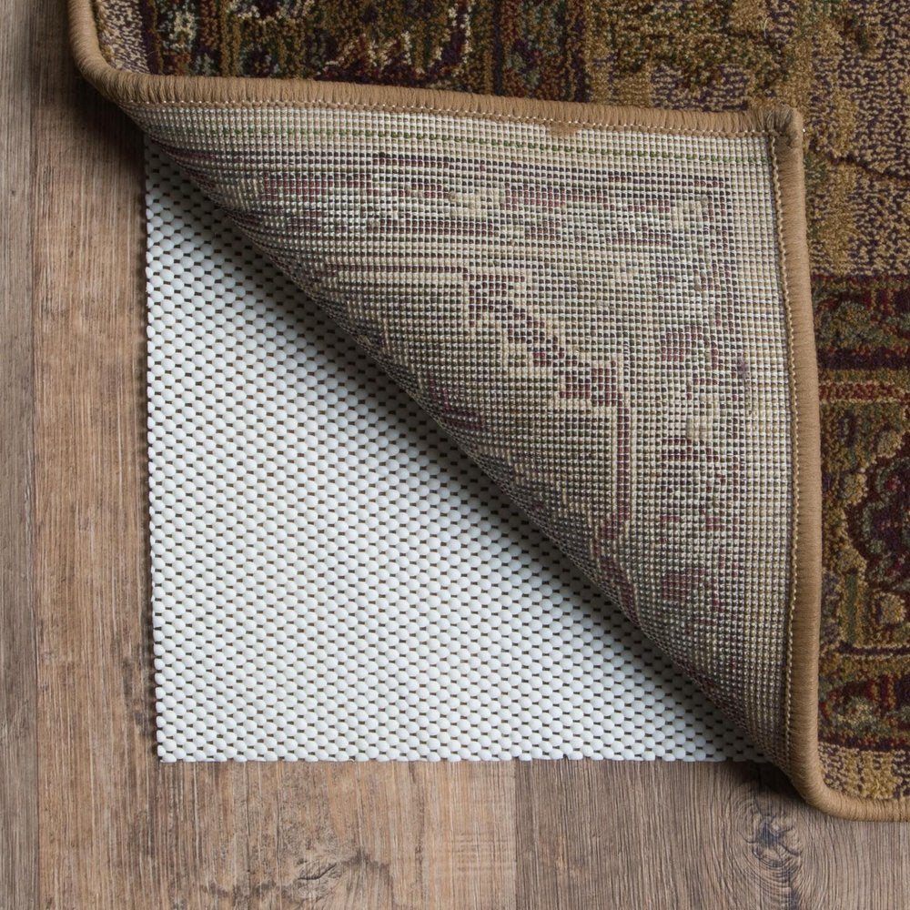 A beige non-slip rug pad is shown under a corner of a patterned rug on a wooden floor.