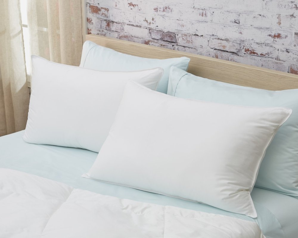 Two white down alternative standard size pillows on a light blue sheet with a white comforter and a brick wall background.