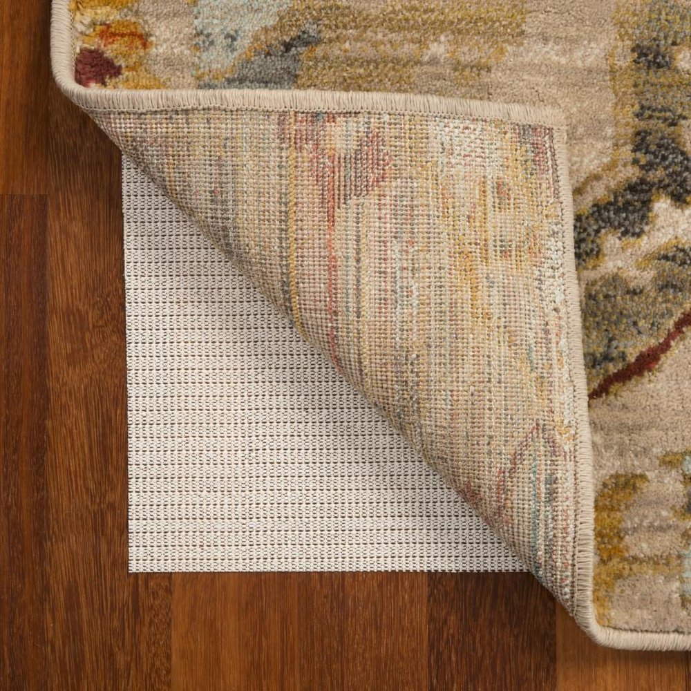 Beige rug pad with textured surface under a beige and multi-colored rug on a wooden floor.