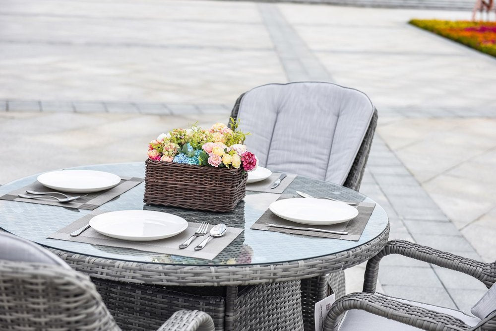 Gray wicker five-piece round glass dining set with floral centerpiece on an outdoor patio.