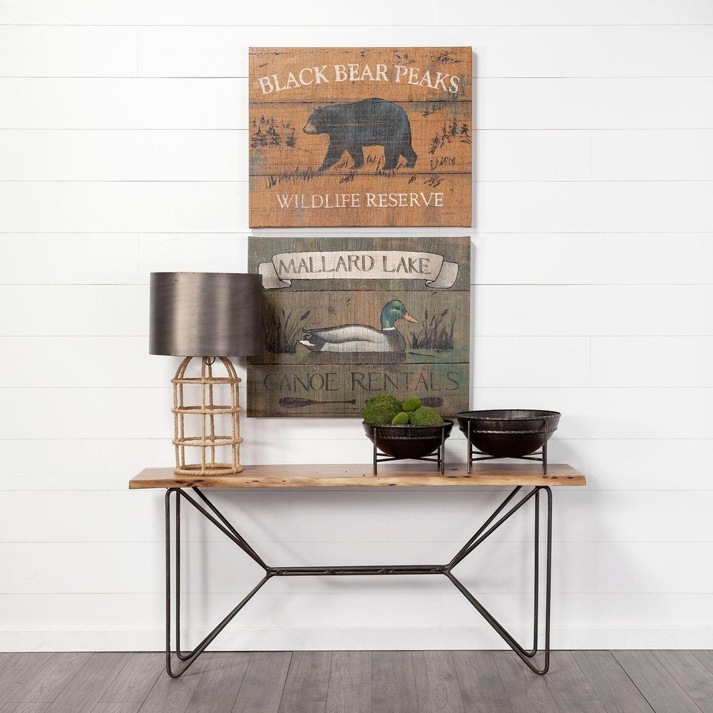 Two black metal decorative bowls on a wooden console table with a lamp and two wall art pieces.