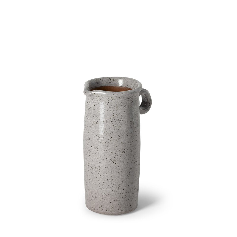 A speckled gray ceramic pitcher with a handle and a pouring spout, filled with a dark liquid, on a white background.