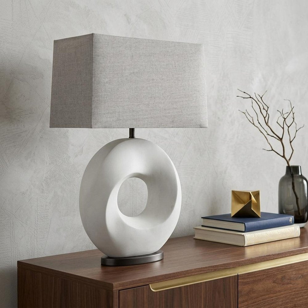 27" White Geometric Table Lamp With Gray Shade displayed on a dark wood tabletop in a furnished interior against a light gray wall.