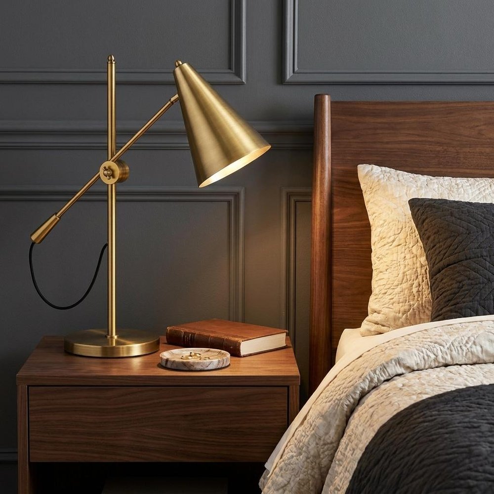 26" Gold Lamp Base LED With Gold Shade styled in a furnished interior with a dark wall on a black floor.