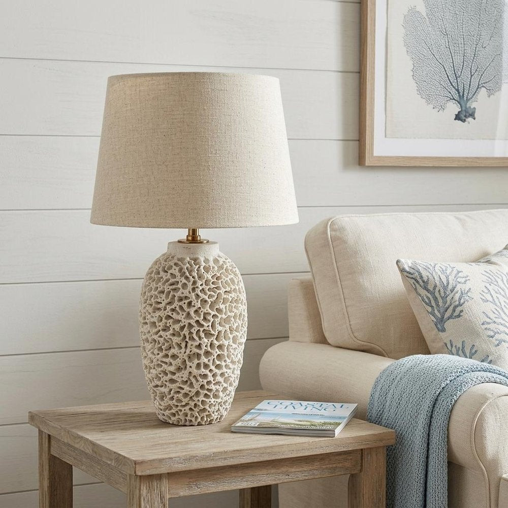 26" Beige Faux Coral Table Lamp With Empire Shade displayed on a wood tabletop in a furnished interior against an off-white wall.