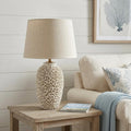 26" Beige Faux Coral Table Lamp With Empire Shade displayed on a wood tabletop in a furnished interior against an off-white wall.